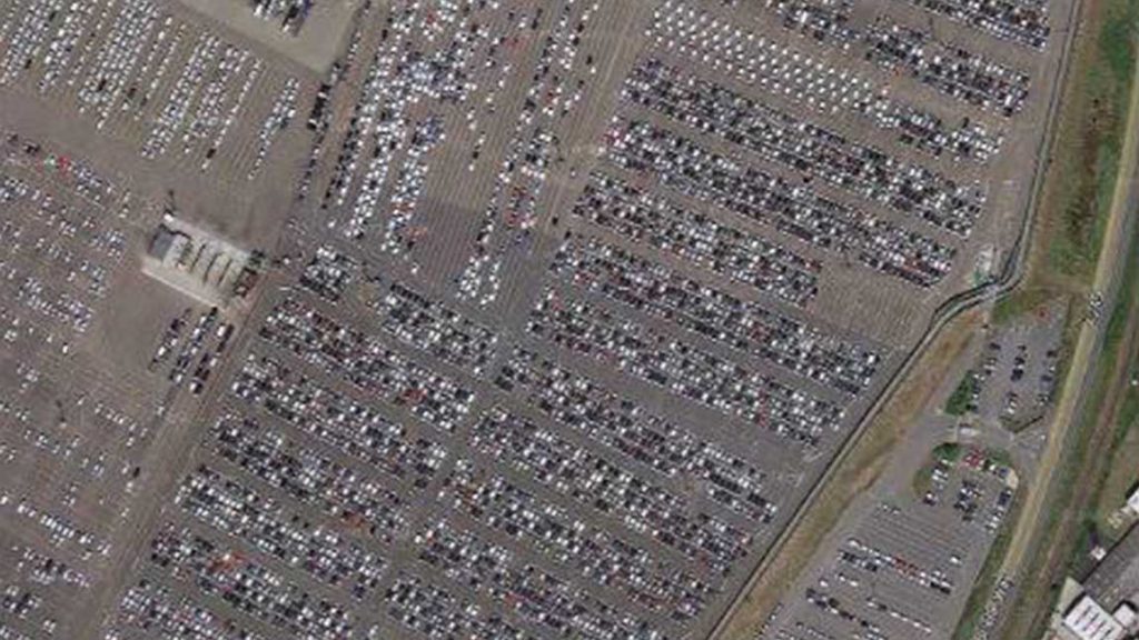 Luftaufnahme von einem vermeidlichen Autofriedhof, der jedoch ein Parkplatz für Neuwagen ist.