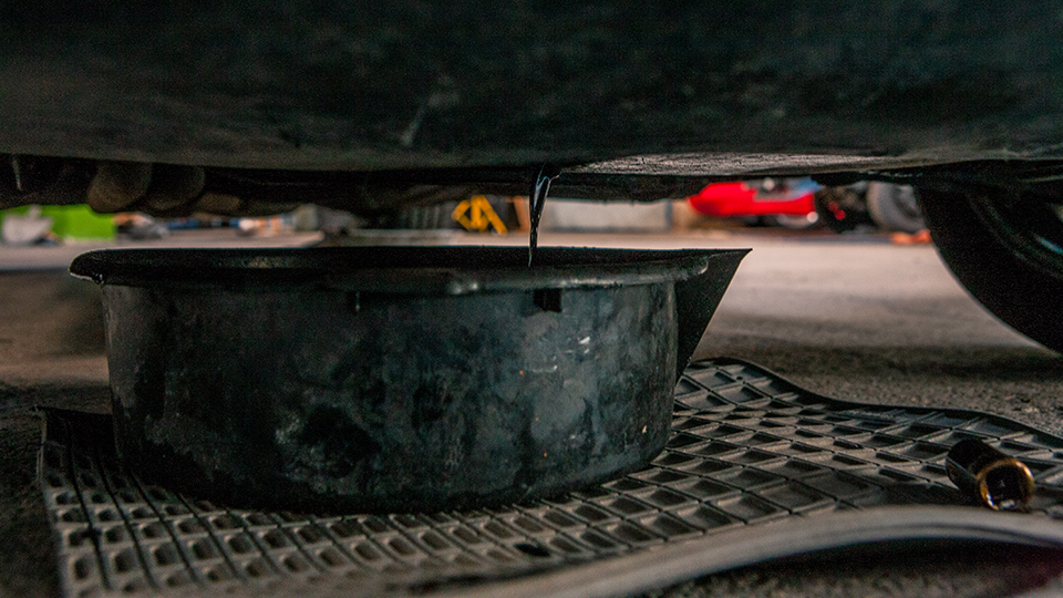 Eine Auffangwanne steht unter einem Auto. Hier wird gerade Altöl abgelassen, danach muss es entsorgt werden und zwar richtig.