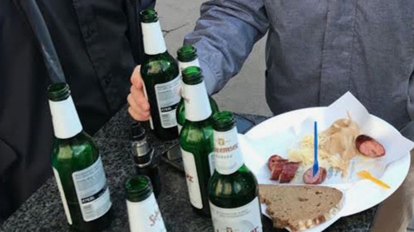 Bierflaschen stehen am Tisch, daneben eine aufgeschnittene Käsekrainer mit Senf und Kren.